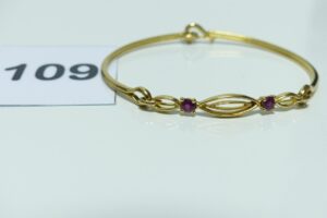 1 bracelet rigide ouvrant en or 750/1000, motif central articulé et orné de 2 petites pierres rouges (diamètre 5/6cm). PB 12,3g