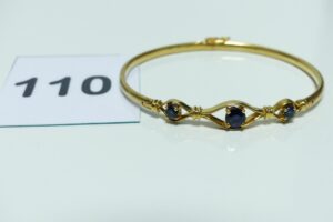 1 bracelet rigide ouvrant en or 750/1000, motif central orné de 3 pierres bleues (diamètre 5/5,5cm). PB 14,5g