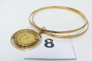 1 bracelet à 2 brins tenus par une breloque serti-griffes un Souverain (diamètre 6,5cm) or 750 et 916/1000. PB 21,8g