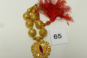 1 Collier à décor de boules ouvragées montées sur cordon en tissu, motif central orné d'une pierre rouge. Le tout en or 875/1000 21k. PB avec cordon 51,5g