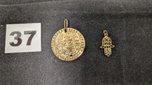 2 Pendentifs, 1 disque décoré d'écriture orientale (abimé, troué) et 1 main de fatma, le tout en or 750/1000 18k. PB 2g